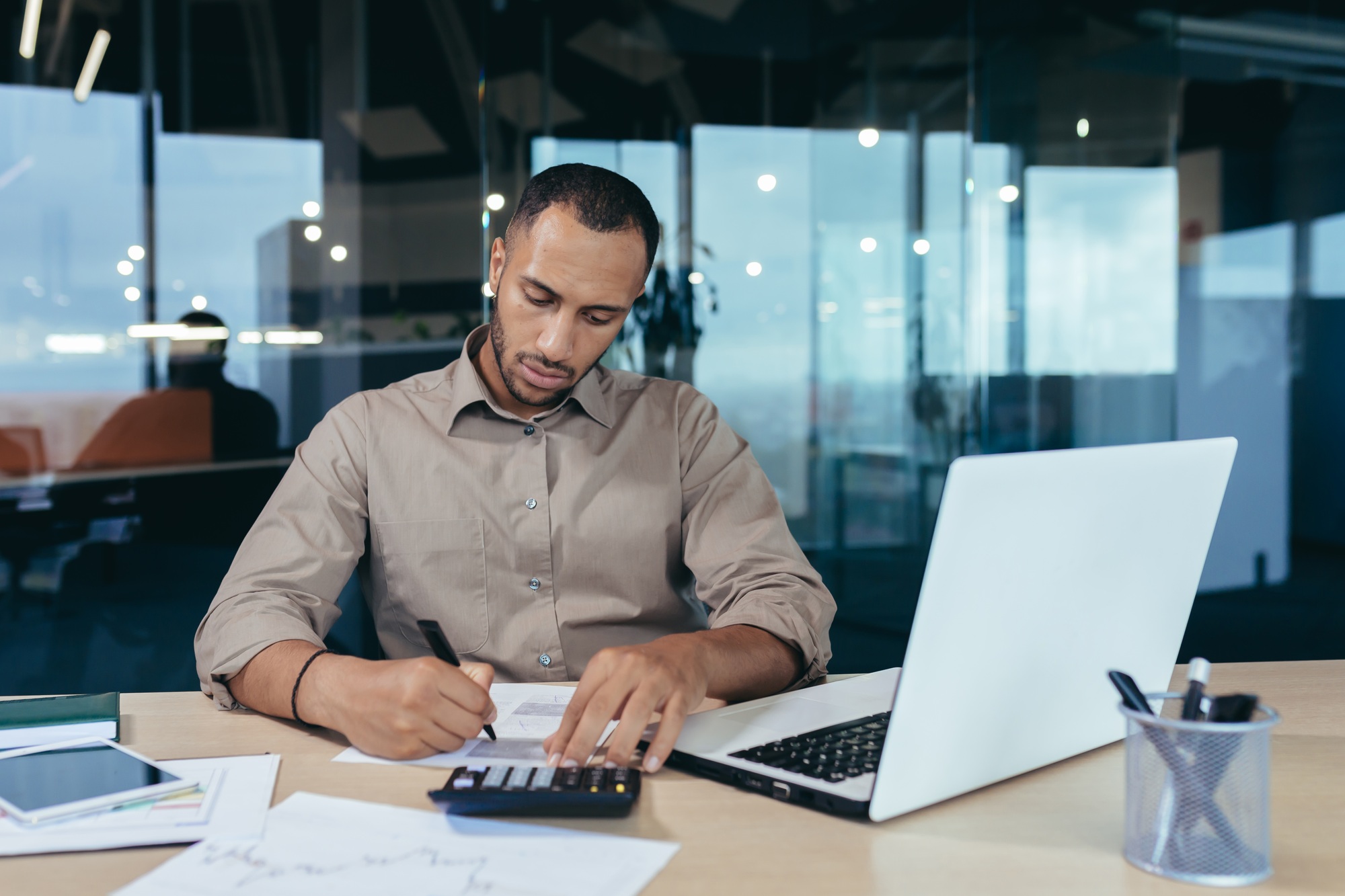 A young African American male auditor, banker working in office at desk with laptop and documents