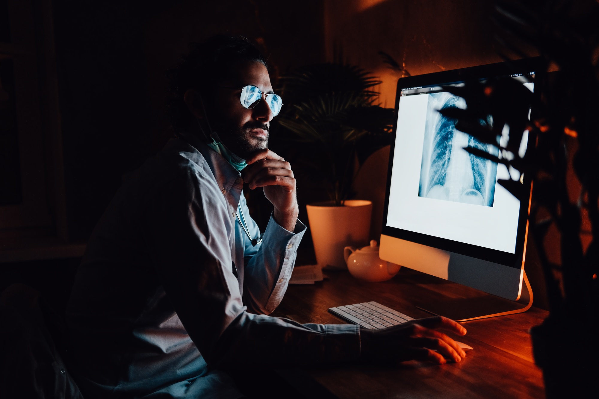Serious doctor with glasses with computer in dark room